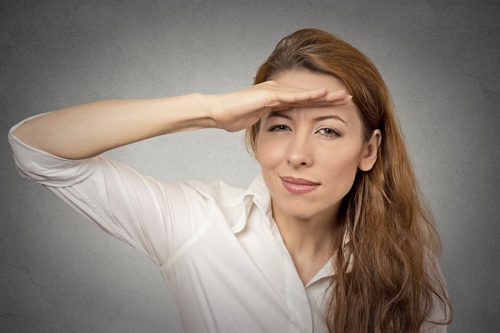 Business woman searching looking far away into future monitoring isolated grey wall office background. Human face expression emotion body language. Future forecast, search, vision, perception concept